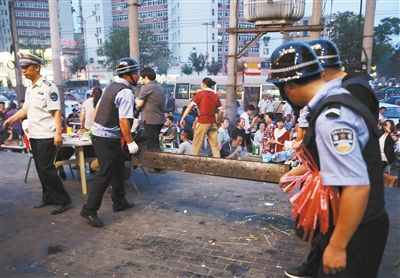 6月13日晚8點，朝陽路和青年路交叉口西側(cè)，一次聯(lián)合執(zhí)法行動中，輔警與協(xié)管抬走商戶的燒烤用具。新京報記者 尹亞飛 攝