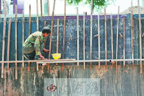 　　烈日下，狹窄的架子上，工人正用錘子固定樁基。