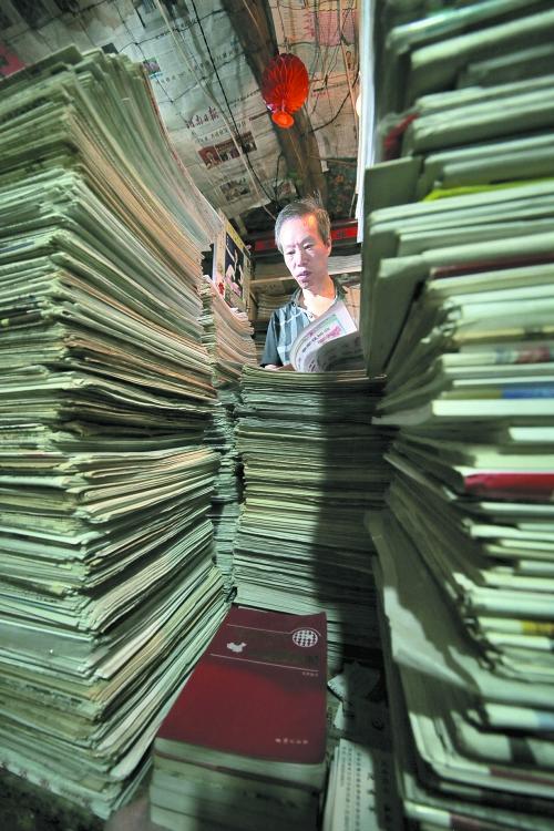 王曉民坐在寫字桌前，被報紙淹沒。