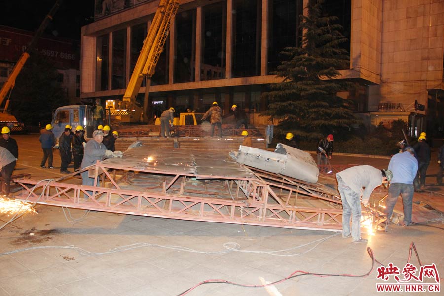 地面上的20多名工人對(duì)吊裝下的廣告牌進(jìn)行分割。