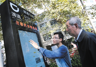 10月15日，滴滴工作人員（左）指導(dǎo)乘客使用“滴滴車站”的電子屏預(yù)約出租車。