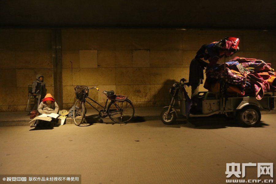 2015年11月8日晚，鄭州，7歲男孩涵洞橋下陪父母練攤，路邊燈下坐小馬扎上寫(xiě)作業(yè)。