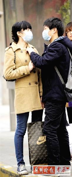 公交站臺(tái)上，一對(duì)年輕人戴著口罩，系緊衣領(lǐng)。